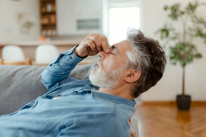 Man holding his nose trying to alleviate headache pain before visiting his primary care physician.